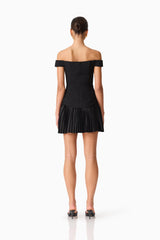 Brunette model wears the Elva Off Shoulder Mini Dress in Black back shot