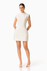Elysia Lace Mini Dress in White with high collar neckline & tulip silhouette posed shot