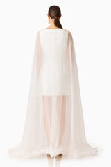 Model wearing the Ellie Cape Mini Dress in White with floor length cape with floral trim back shot