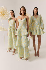 Brunette model wearing the Penelope Asymmetrical Gown in Yellow & Blue Floral campaign shot